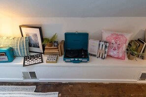 Een plank met diverse objecten, waaronder een cassette speler, een ingelijste foto, boeken en decoratieve kussens.