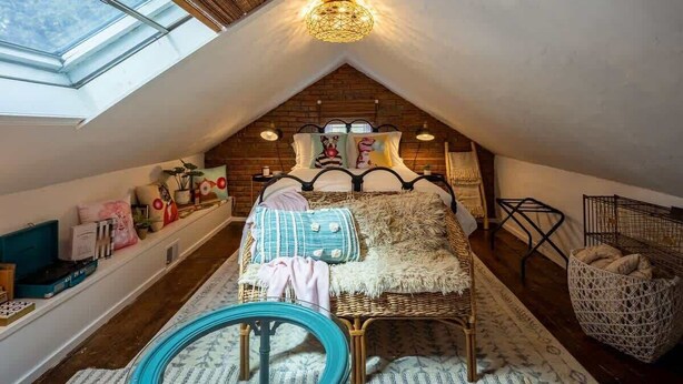 Ein gemütliches Schlafzimmer im Dachgeschoss mit schrägen Wänden, einem Bett mit Kopfteil, einem Oberlicht und einem Korb auf dem Boden.