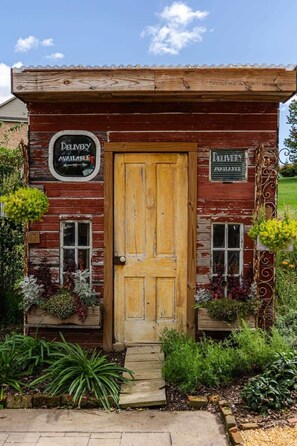 A rustic wooden building with a wooden door, two windows, and signs indicating delivery is available.