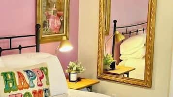 Een slaapkamer met een bed, een nachtkastje met een lamp, een spiegel en een lijst met een foto aan de muur.