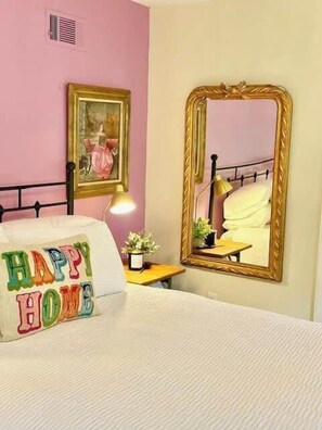 Een slaapkamer met een bed, een nachtkastje met een lamp, een spiegel en een lijst met een foto aan de muur.