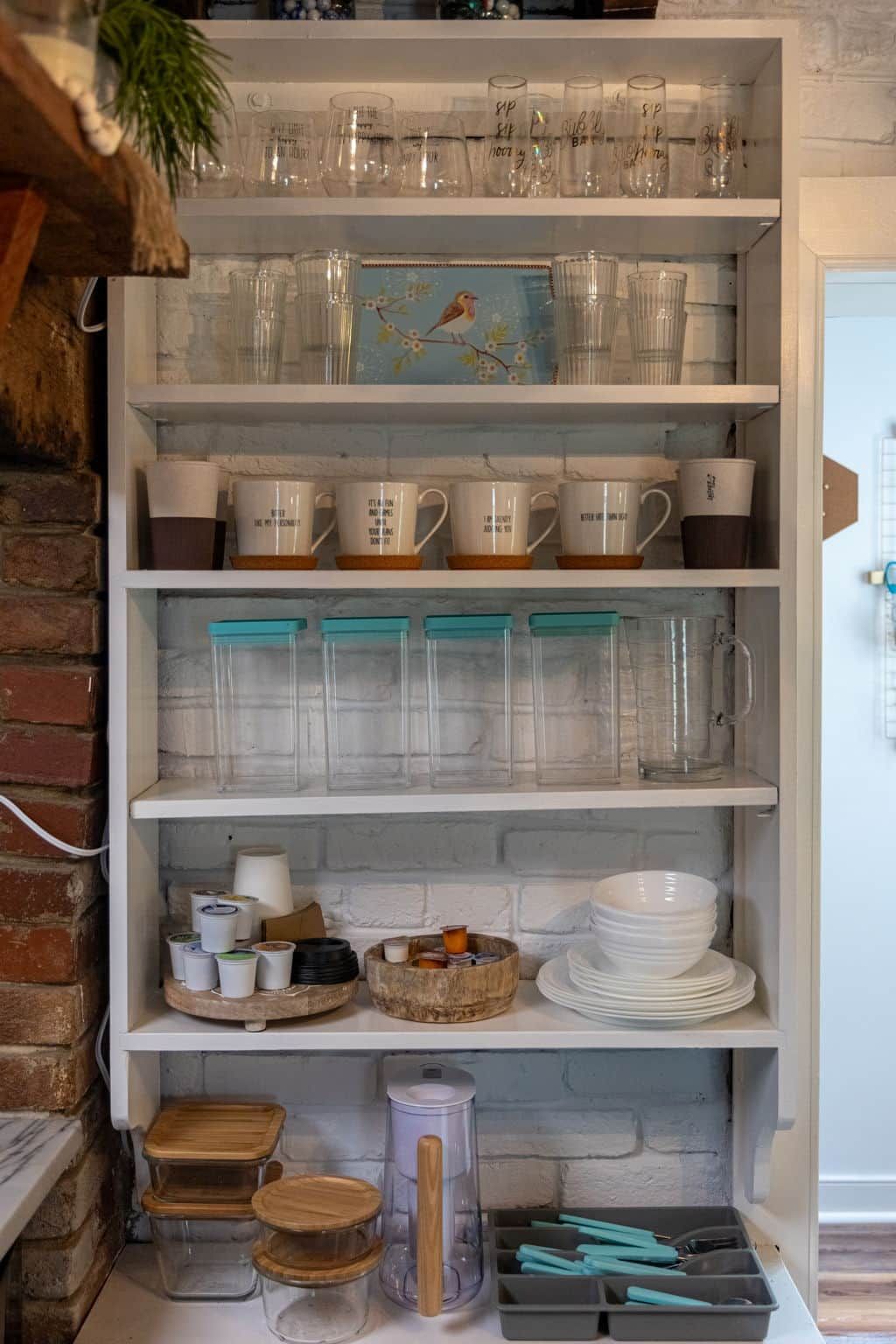 A kitchen shelf with various glassware, mugs, and storage containers.