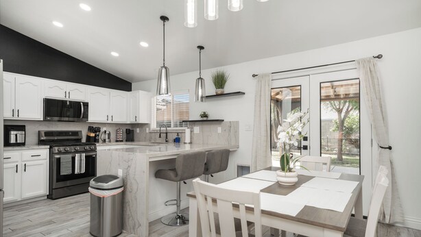 A modern kitchen with white cabinets, a built-in oven, a microwave, and a stainless steel trash can.