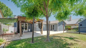 A backyard with a pergola, a tree, and a house.