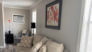 A living room with a beige sectional sofa, a framed floral artwork, and a wooden floor.