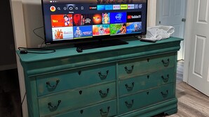 A television on a teal dresser displaying a streaming service interface with various shows and movies.