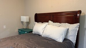 A neatly made bed with a dark brown headboard, white pillows, and a teal nightstand with a white lamp.