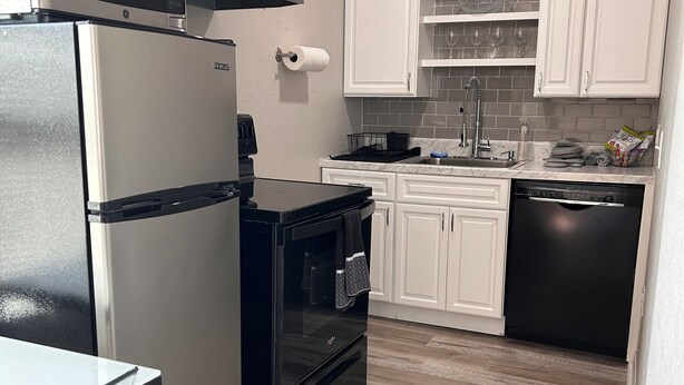 A modern kitchen with white cabinets, a stainless steel refrigerator, a black oven, and a dishwasher.