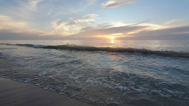 Une plage avec des vagues et un coucher de soleil.