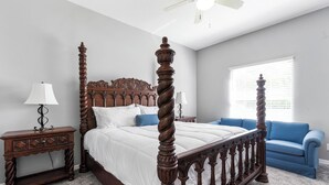 Une chambre à coucher avec un lit à baldaquin, une table de chevet, un canapé bleu et un ventilateur de plafond.