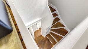 Una escalera estrecha con escalones de madera y paredes blancas.