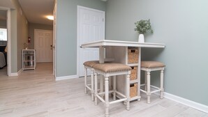 Une pièce dotée d’un parquet en bois de couleur claire, d’une porte blanche et d’une petite table blanche accompagnée de deux tabourets rembourrés.