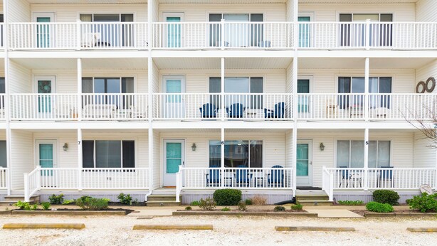 Un immeuble à plusieurs étages, aux murs extérieurs blancs et doté de balcons. Chaque étage est pourvu d’une série de fenêtres et de portes, et certains balcons sont aménagés avec du mobilier.