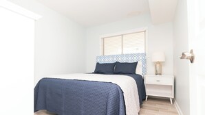 Une chambre à coucher avec un lit, une table de chevet, une lampe et une fenêtre avec des stores.