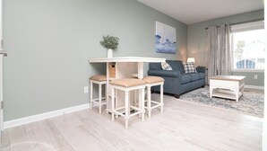 Un salon doté d’un parquet en bois de couleur claire, d’un canapé bleu, d’une petite table blanche et d’une plante décorative.