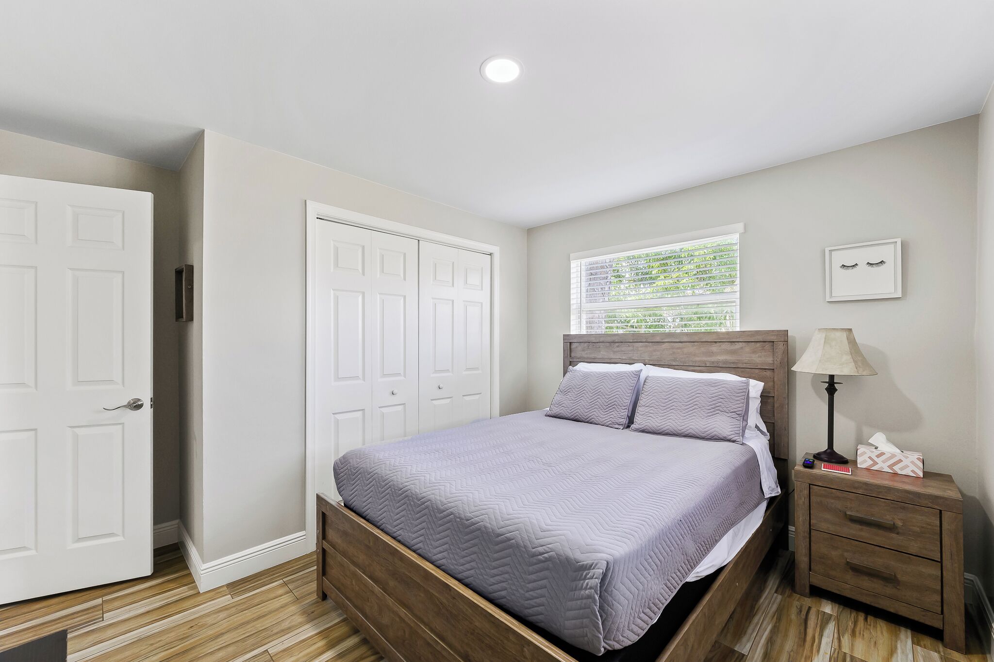 A bedroom with a bed, nightstand, lamp, and window.