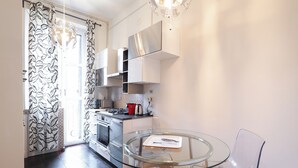A modern kitchen with white cabinets, a glass dining table, and a black and white patterned door. - C23 - Premium Apartment in Milan (Milano)
