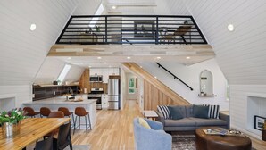 A spacious loft with a high ceiling, a mezzanine level, a kitchen with modern appliances, and a cozy seating area with a sofa and ottoman. - Brand NEW build. A-frame 2bed+/2bath. Nature paradise. Pepin, WI. (Pepin)