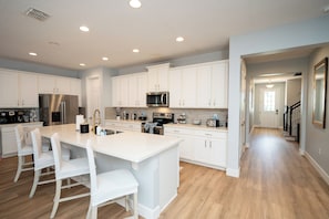 A modern kitchen with white cabinetry, stainless steel appliances, and a central island with seating.