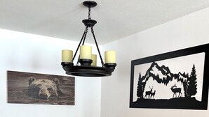 Un comedor con una mesa y sillas de madera, una araña y dos cuadros en la pared.