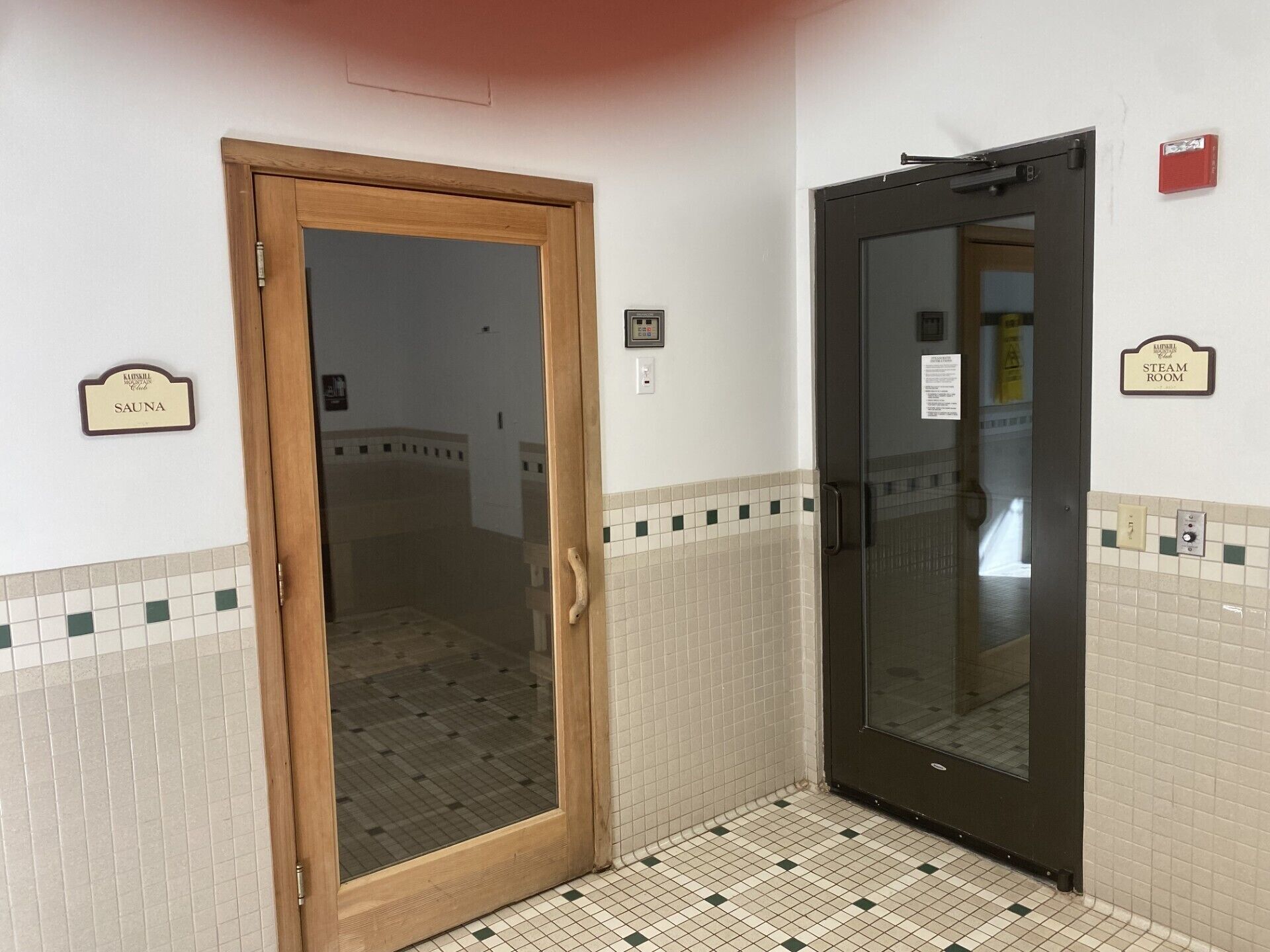 A hallway with a wooden door labeled "SAUNA" and a black door labeled "STEAM ROOM".