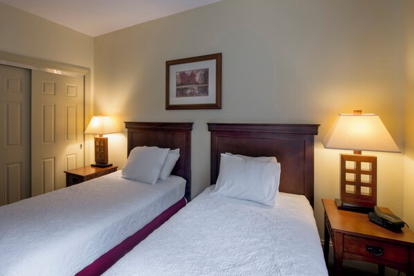 A hotel room with two beds, a framed picture on the wall, and a nightstand with a lamp and remote control.