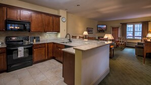 A kitchen with wooden cabinets, a microwave, an oven, and a large island with a sink. There is a dining area with a table and chairs, and a television mounted on the wall. - The ultimate resort experience. Pool, hot tub, sauna, steam room, exercise room. (Hunter)