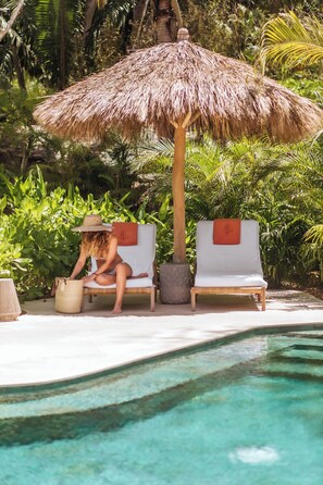 A poolside area with two lounge chairs, one with a straw hat and a bag, and a thatched umbrella. - Naviva, A Four Seasons Resort, Punta Mita, Mexico - All Inclusive (Punta de Mita)