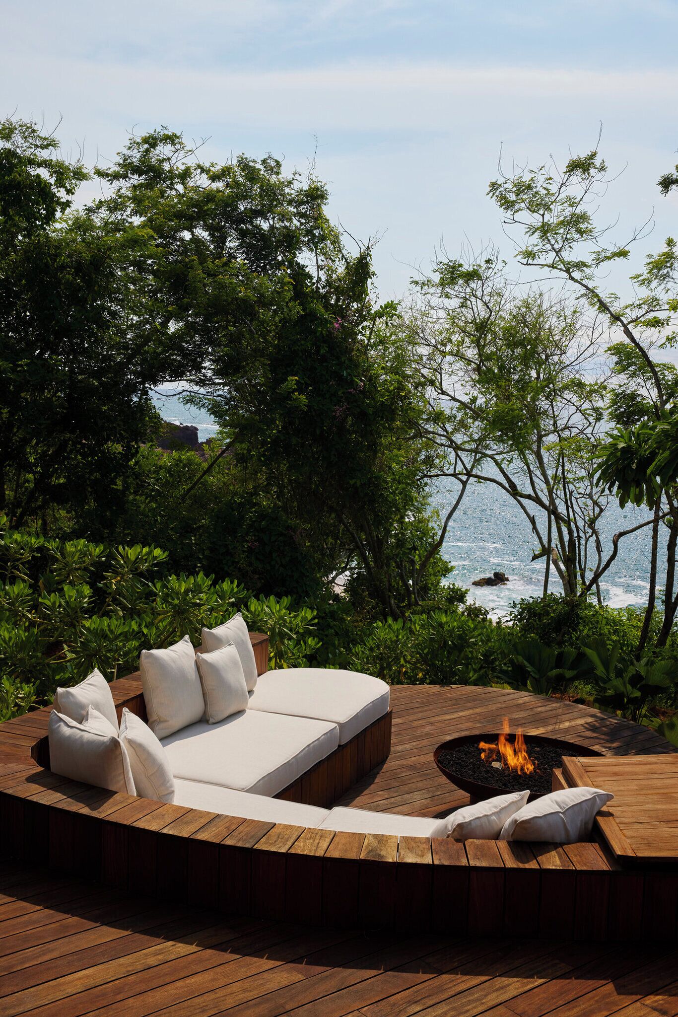 An outdoor seating area with a wooden deck, a sofa with cushions, and a fire pit.