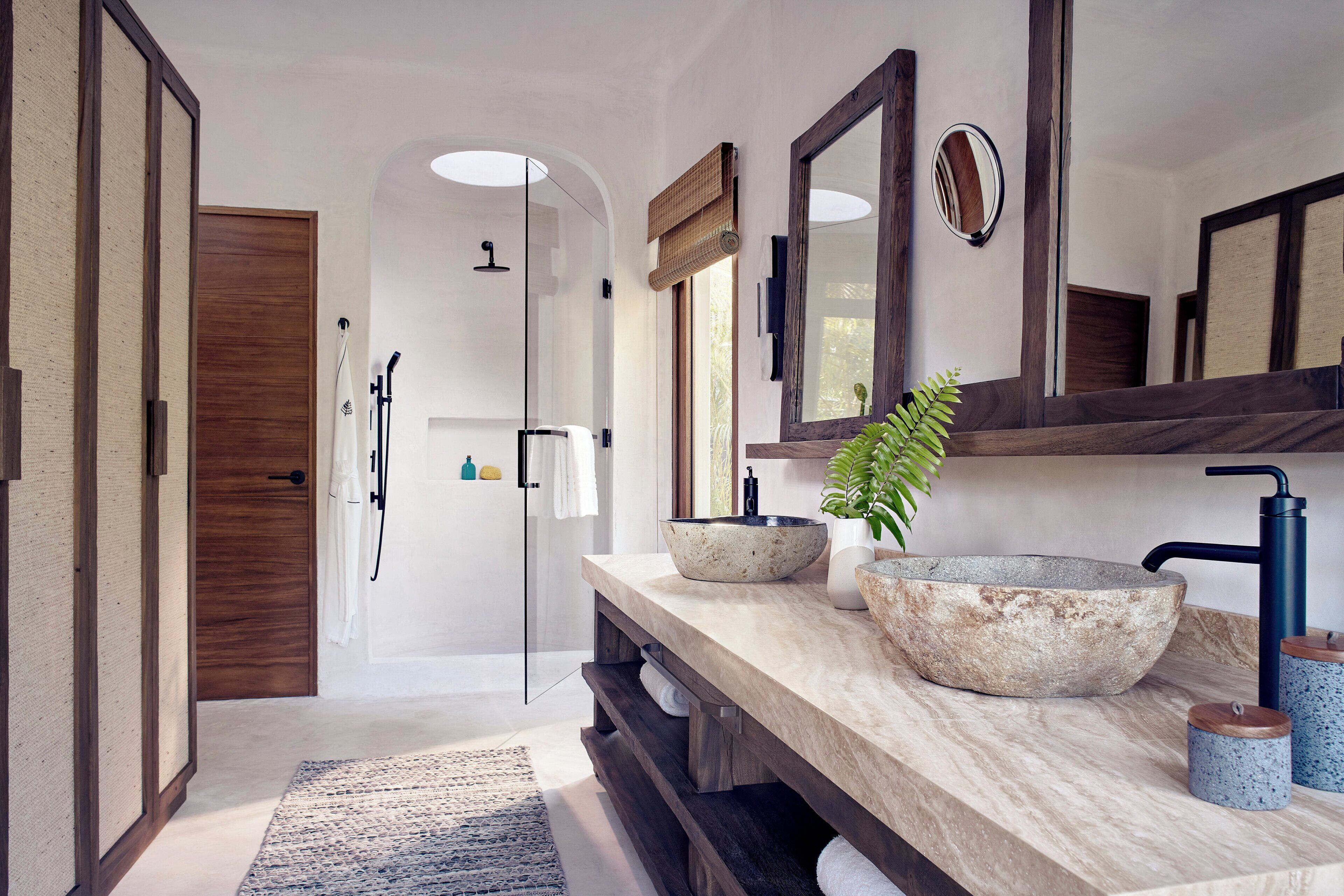 A modern bathroom with a large mirror, two stone sinks, and a shower area.