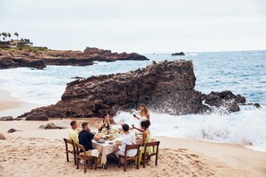A group of people dining at a table on a beach with rocky formations and the ocean in the background. - Naviva, A Four Seasons Resort, Punta Mita, Mexico - All Inclusive (Punta de Mita)