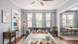 A bedroom with a bed, a ceiling fan, a bookshelf, a desk, and a dining area.