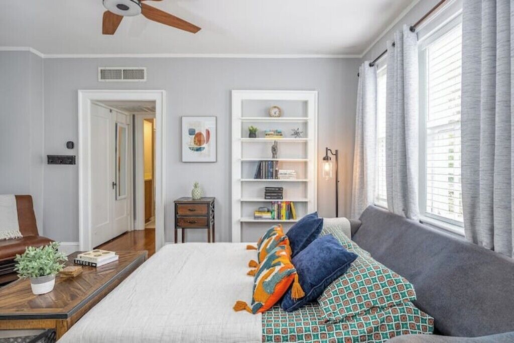 A bedroom with a bed, a bookshelf, a desk, and a window with curtains.