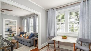 A living room with a gray sofa, a coffee table, a side table, a bookshelf, and a window with curtains.
