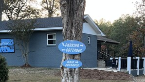 A directional sign on a tree with arrows pointing to 'Parking', 'Cottages', and 'Main Entrance'. - Sapphire 2BR/2Bath Module Cottage at Blue Hollow (Hattiesburg)