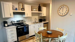 A kitchen with white cabinets, a stove, a microwave, and a wooden dining table with chairs. - Sapphire 2BR/2Bath Module Cottage at Blue Hollow (Hattiesburg)