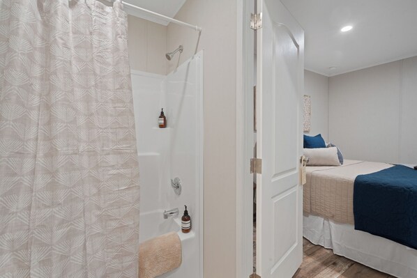 A bedroom with a bed, a bedside table, and a bathroom with a shower.