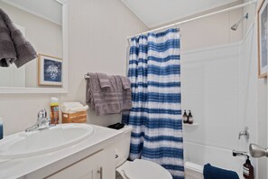 A bathroom with a white sink, a toilet, a shower with a blue and white striped curtain, and a towel rack with towels.