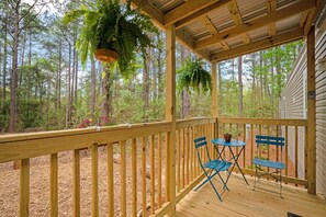 A wooden deck with a metal railing, two blue folding chairs, and hanging plants. - Sapphire 2BR/2Bath Module Cottage at Blue Hollow (Hattiesburg)