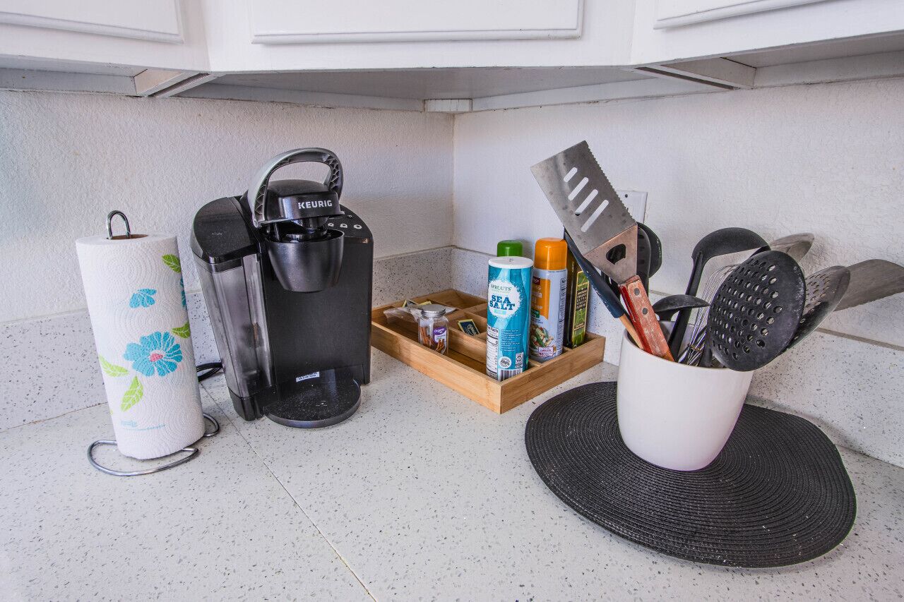 A kitchen area with a coffee maker, a paper towel holder, a spice rack, and a cutting board.