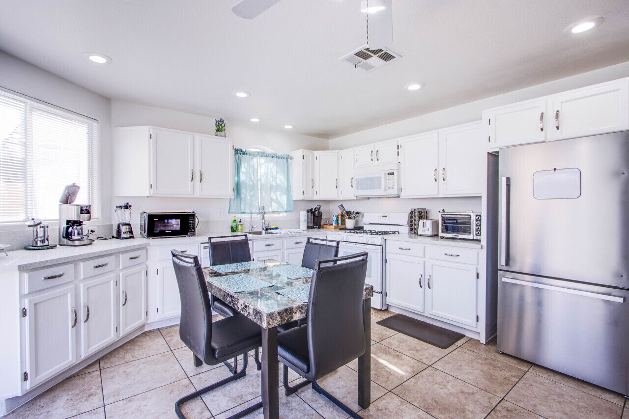 A modern kitchen with white cabinets, a granite countertop, a dining table with chairs, and stainless steel appliances.