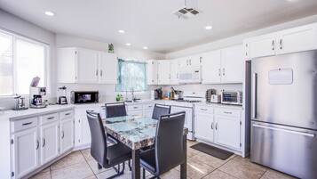 A modern kitchen with white cabinets, a granite countertop, a dining table with chairs, and stainless steel appliances.
