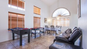 Un grand espace de vie comprenant une table de baby-foot, une table à manger avec des chaises et un canapé en cuir.