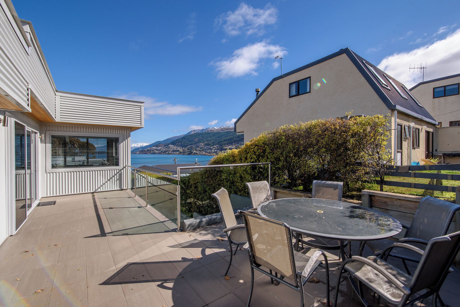 A patio with a table and chairs, overlooking a body of water and mountains.