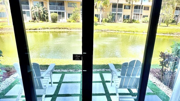 Vista através de uma porta de vidro de uma área de piscina com cadeiras e uma placa com a mensagem 'Cuidado com o degrau'.