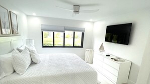 Quarto moderno com uma cama grande, televisão na parede e janela com persianas.