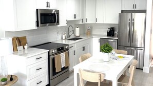 Cozinha moderna com armários brancos, eletrodomésticos de aço inoxidável e uma ilha central com assentos.