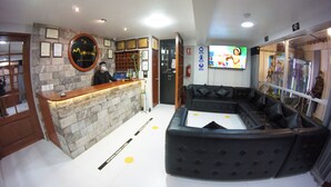 Ein Empfangsbereich mit Steinwand, Holzbude, schwarzem Ledersofa und einem Fernsehbildschirm.
