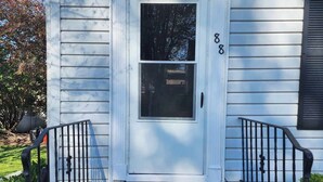 A white house with a black door, a small porch, and a welcome mat.