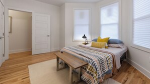 A bedroom with a bed, bedside table, bench, and a door leading to another room.